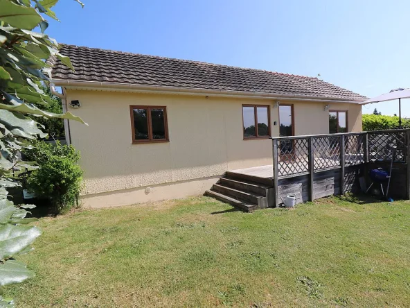Bungalow with wooden deck and garden in sunlight.