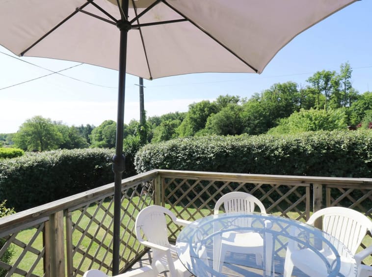 Terrasse avec parasol et chaises donnant sur la verdure.