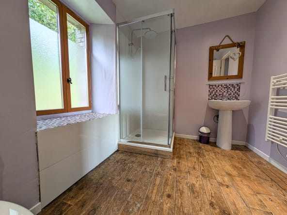 Modern bathroom with shower, wooden floor, and window.