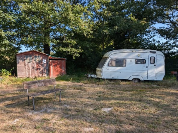 Caravan beside wooden shed in forest clearing.
