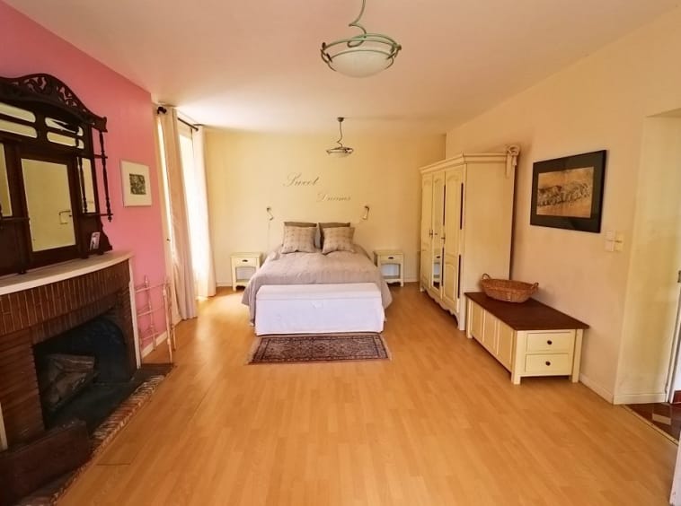 Spacious bedroom with fireplace and wooden flooring.