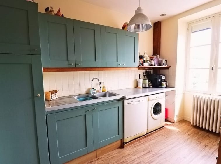 Modern kitchen with green cabinets and wooden floor.